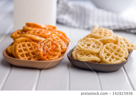 Two Bowls of Waffle Fries and Potato Snacks. Spicy and Classic Seasoned Chips on Table Two Bowls of Waffle Fries and Potato Snacks. Spicy and Classic Seasoned Chips on Table 142823936