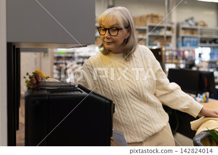 Mature woman examining a coffee maker in a modern appliance store 142824014