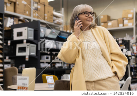 Senior woman shopping in a store, talking on a mobile phone Senior woman shopping in a store, talking on a mobile phone 142824016