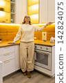 Woman standing in modern kitchen showroom, looking at upper cabinets 142824075