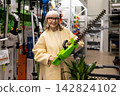 Senior woman smiling, holding a hedge trimmer and shopping in a hardware store 142824102