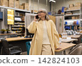 Senior woman talking on phone while shopping for furniture in a modern retail store 142824103
