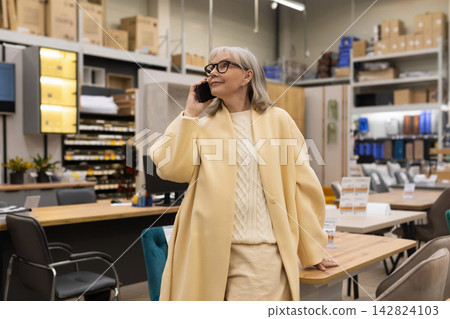 Senior woman talking on phone while shopping for furniture in a modern retail store 142824103