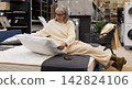 Mature woman testing a pillow on a mattress while shopping for home goods 142824106