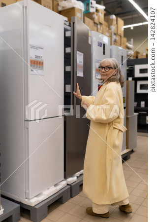 Senior woman considering refrigerators in a large retail appliance store Senior woman considering refrigerators in a large retail appliance store 142824107