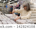 Senior woman shopping for wallpaper, making a choice in a home improvement store 142824108