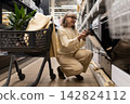 Senior woman shopping for new home appliances, checking an oven in a retail store 142824112