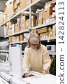 Senior woman examining household appliance details in a busy store aisle 142824113