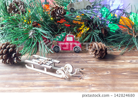 Wooden toy sled and a red toy truck with "Merry Christmas" text on a wooden table with pine branches Wooden toy sled and a red toy truck with "Merry Christmas" text on a wooden table with pine branches 142824680