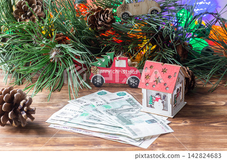Russian ruble banknotes next to a toy house and a red toy truck on a wooden table with pine branches. Russian ruble banknotes next to a toy house and a red toy truck on a wooden table with pine branches. 142824683