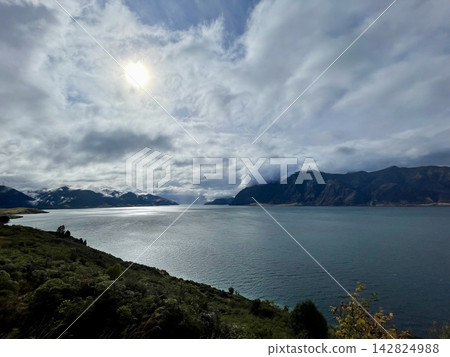 陽光穿透雲層,映照出波光粼粼的湖面和巍峨的山脈,景色令人嘆為觀止。 陽光穿透雲層,映照出波光粼粼的湖面和巍峨的山脈,景色令人嘆為觀止。 142824988