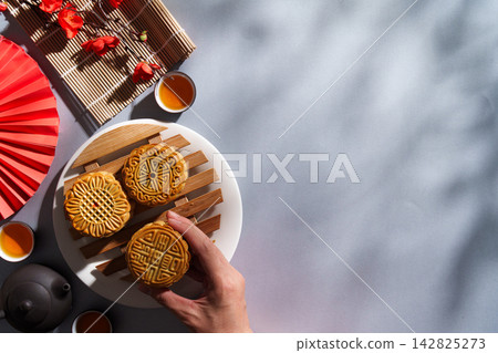 Cropped hand holding mooncake with teapot and cups for Mid-Autumn Festival Cropped hand holding mooncake with teapot and cups for Mid-Autumn Festival 142825273