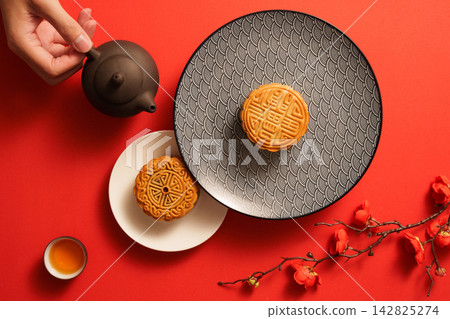 Flat lay of hand pouring tea beside traditional mooncakes on red background Flat lay of hand pouring tea beside traditional mooncakes on red background 142825274