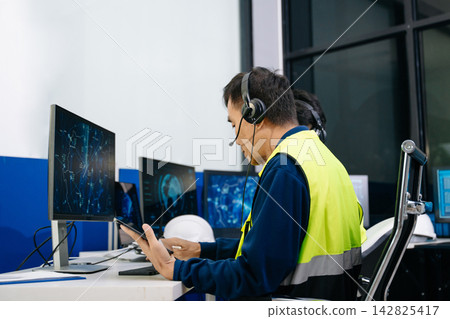 Mature Asian industrial dispatcher in a safety vest and headset analyzing global logistics data on digital screens Mature Asian industrial dispatcher in a safety vest and headset analyzing global logistics data on digital screens 142825417