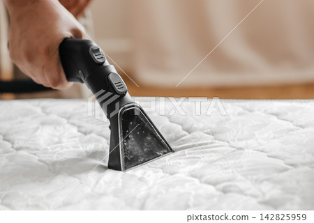 Close up of professional mattress cleaning with extraction vacuum cleaner nozzle Close up of professional mattress cleaning with extraction vacuum cleaner nozzle 142825959