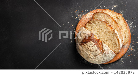 Freshly baked round artisan bread loaf with sliced pieces displayed on a wooden board against a dark background with flour scattered around. copy space. Freshly baked round artisan bread loaf with sliced pieces displayed on a wooden board against a dark background with flour scattered around. copy space. 142825972
