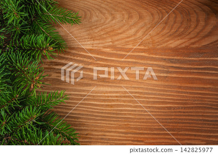 Evergreen pine branches arranged on a rustic wooden surface, creating a natural frame with a warm, textured background suitable for seasonal decorations Evergreen pine branches arranged on a rustic wooden surface, creating a natural frame with a warm, textured background suitable for seasonal decorations 142825977
