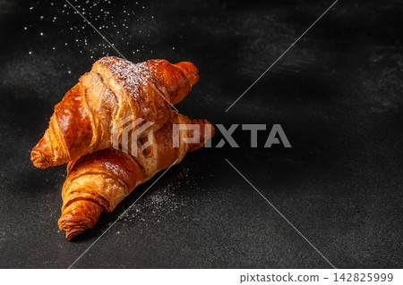 Freshly baked golden croissants dusted with powdered sugar on a dark textured surface, showcasing flaky layers and a delicious appearance Freshly baked golden croissants dusted with powdered sugar on a dark textured surface, showcasing flaky layers and a delicious appearance 142825999