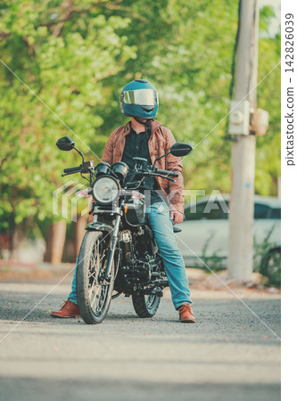 Young dotorcyclist wearing a helmet, parked on the road and looking at side Young dotorcyclist wearing a helmet, parked on the road and looking at side 142826039