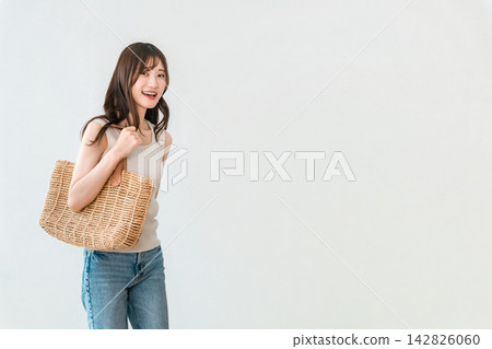 一位年輕女子微笑著拎著草編包出門。這是夏日休閒時尚的體現。 一位年輕女子微笑著拎著草編包出門。這是夏日休閒時尚的體現。 142826060