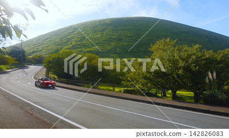 A red sports car (Mazda) drives along a road near Mt. Omuro (Izu Kogen) in early autumn. A red sports car (Mazda) drives along a road near Mt. Omuro (Izu Kogen) in early autumn. 142826083