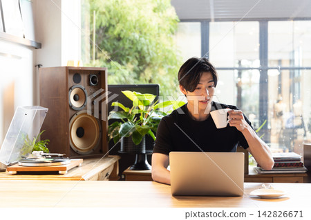 A man working on his computer while drinking coffee. 142826671