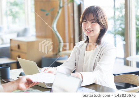 一位商人和一位女商人隔著辦公桌交換文件。 142826676