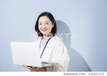 一位女上班族面帶微笑,手持筆記型電腦;她是一位在工作中運用數位科技的日本女商人。 一位女上班族面帶微笑,手持筆記型電腦;她是一位在工作中運用數位科技的日本女商人。 142827115
