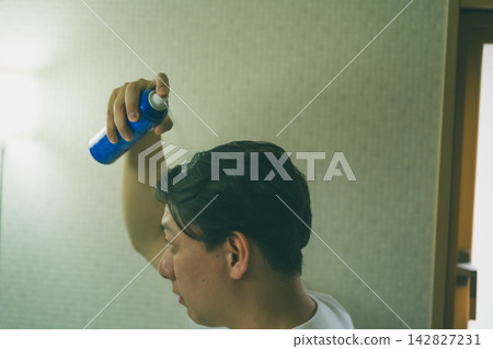 A profile view of a man in his 40s using hair growth spray for scalp care. A profile view of a man in his 40s using hair growth spray for scalp care. 142827231