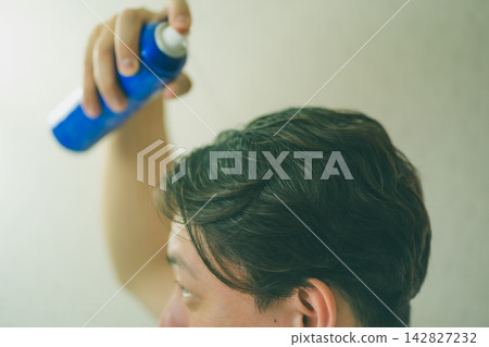 A man in his 40s sprays hair growth spray from above his head. A man in his 40s sprays hair growth spray from above his head. 142827232