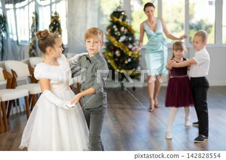 Christmas ball - group of preteen children in festive clothes dances a foxtrot near New Year tree Christmas ball - group of preteen children in festive clothes dances a foxtrot near New Year tree 142828554