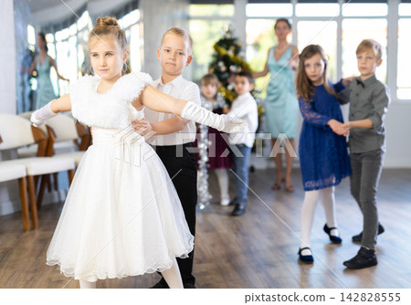 Preteen children in elegant outfits practicing partner dance in Christmas studio Preteen children in elegant outfits practicing partner dance in Christmas studio 142828555