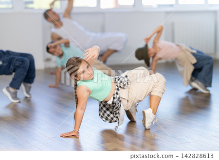 Smiling sports teen girl performing krump movements on floor with group children in breakdance studio with male coach Smiling sports teen girl performing krump movements on floor with group children in breakdance studio with male coach 142828613