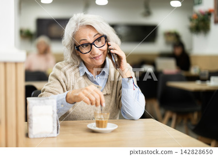 Senior woman spends time at table in cafe, talking on phone Senior woman spends time at table in cafe, talking on phone 142828650