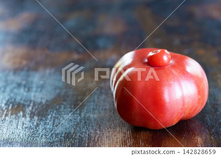 Ripe and red unusual ugly tomato with small tomato growing naturally on top of its larger body, creating strikingly irregular form, on rustic wooden surface. Concept for imperfect produce Ripe and red unusual ugly tomato with small tomato growing naturally on top of its larger body, creating strikingly irregular form, on rustic wooden surface. Concept for imperfect produce 142828659