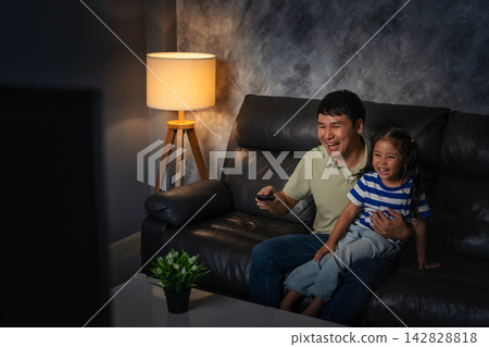 funny father and daughter laughing while watching comedy film on tv in the living room at night funny father and daughter laughing while watching comedy film on tv in the living room at night 142828818