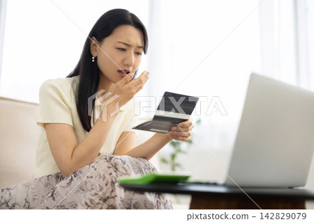 A young Japanese woman smiles while looking at her bankbook. 142829079