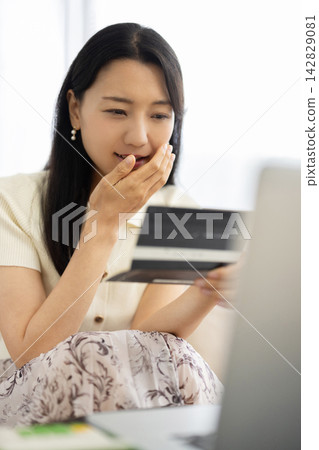 一位年輕的日本女子看著她的存摺，臉上露出笑容。 142829081