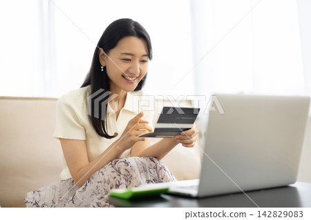 A young Japanese woman smiles while looking at her bankbook. 142829083