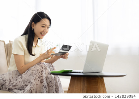 A young Japanese woman smiles while looking at her bankbook. A young Japanese woman smiles while looking at her bankbook. 142829084