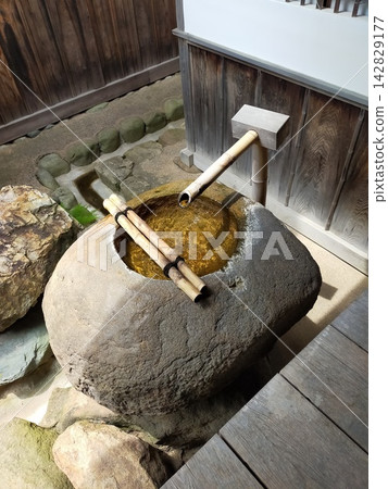 日本花園中迷人的築拜(石盆)和水盆;清澈的泉水從竹管流出,水盆由石頭製成。 日本花園中迷人的築拜(石盆)和水盆;清澈的泉水從竹管流出,水盆由石頭製成。 142829177