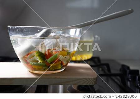 Cooling blanched vegetables in ice water in a glass bowl on a wooden cutting board Cooling blanched vegetables in ice water in a glass bowl on a wooden cutting board 142829300