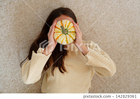 Teen girl lying on carpet holding decorative pumpkin at home 142829361