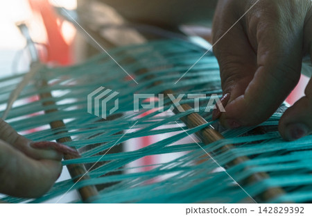 Woman hands arranging green cotton thread on a traditional handloom during weaving, handmade textile production. Artisan craftsmanship, skill, fabric making and cultural heritage. Sustainable craft. Woman hands arranging green cotton thread on a traditional handloom during weaving, handmade textile production. Artisan craftsmanship, skill, fabric making and cultural heritage. Sustainable craft. 142829392