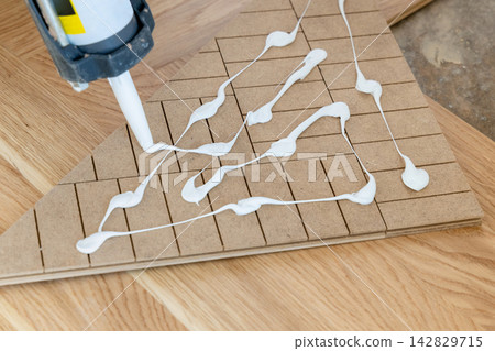 Herringbone parquet installation, white adhesive applied to an oak parquet piece top view Herringbone parquet installation, white adhesive applied to an oak parquet piece top view 142829715