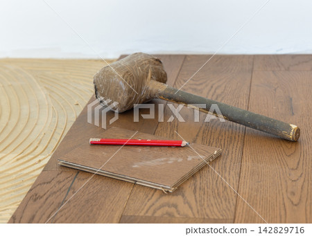 Rubber mallet and pencil on brown oak parquet planks during hardwood flooring installation 142829716
