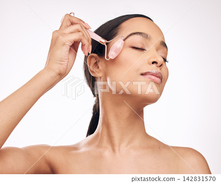 Female model, studio and beauty with derma roller for skin surface or pigmentation, skincare or cosmetic. Young woman, white background and massage with tool on cheek for wellness, glow and shine Female model, studio and beauty with derma roller for skin surface or pigmentation, skincare or cosmetic. Young woman, white background and massage with tool on cheek for wellness, glow and shine 142831570