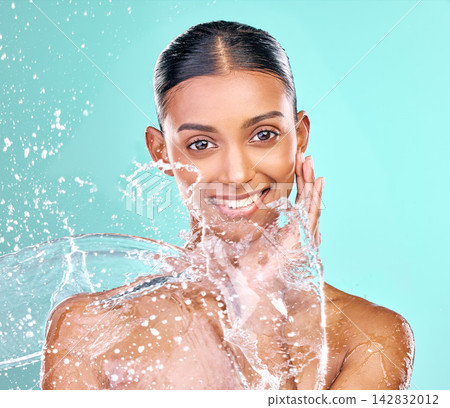 Woman face, washing and water splash for skincare, hygiene and beauty or dermatology in studio. Indian model in portrait with liquid for natural, cosmetics and facial cleaning on blue background Woman face, washing and water splash for skincare, hygiene and beauty or dermatology in studio. Indian model in portrait with liquid for natural, cosmetics and facial cleaning on blue background 142832012