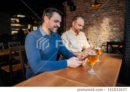 Two men focusing on smartphones while drinking beer at bar Two men focusing on smartphones while drinking beer at bar 142832637