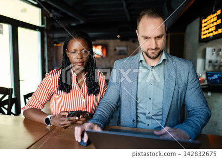 Colleagues working together at a cafe, using a laptop and smartphone Colleagues working together at a cafe, using a laptop and smartphone 142832675